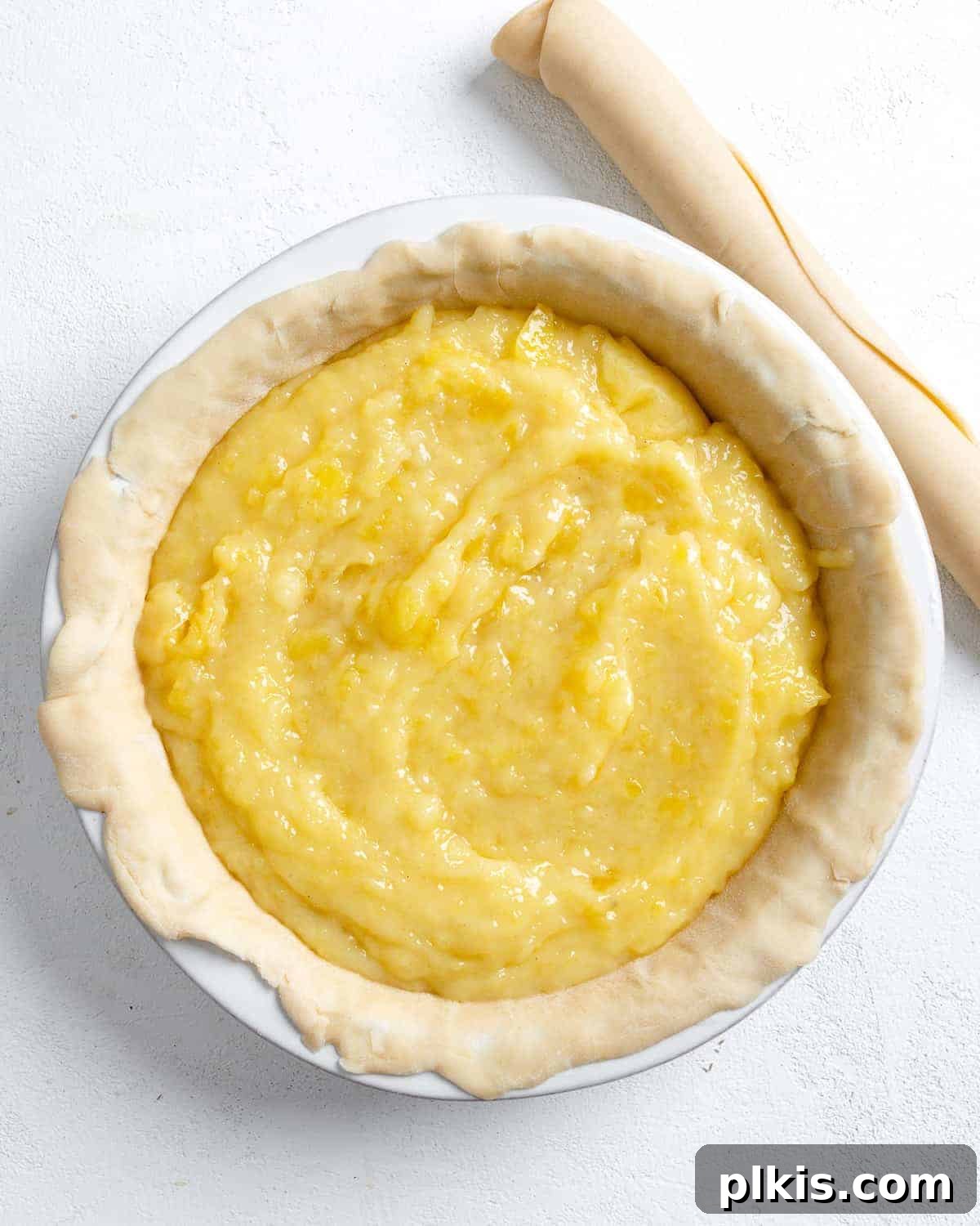 Tropical Vegan Coconut Pineapple Pie 10 Process shot of the creamy pineapple filling being poured into the pie crust set in a mold, against a white background.