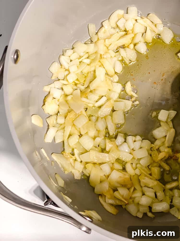 Rustic Cabbage and Bean Pot 4 Process shot of cooking diced onion and sliced garlic in a large pot with olive oil.