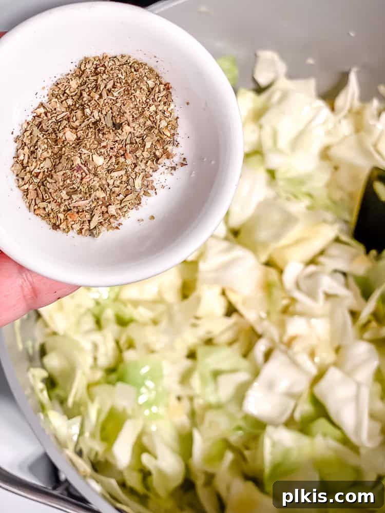 Rustic Cabbage and Bean Pot 5 Process shot of adding Italian seasoning, salt, and pepper to sautéed onions, garlic, and cabbage in a pot.