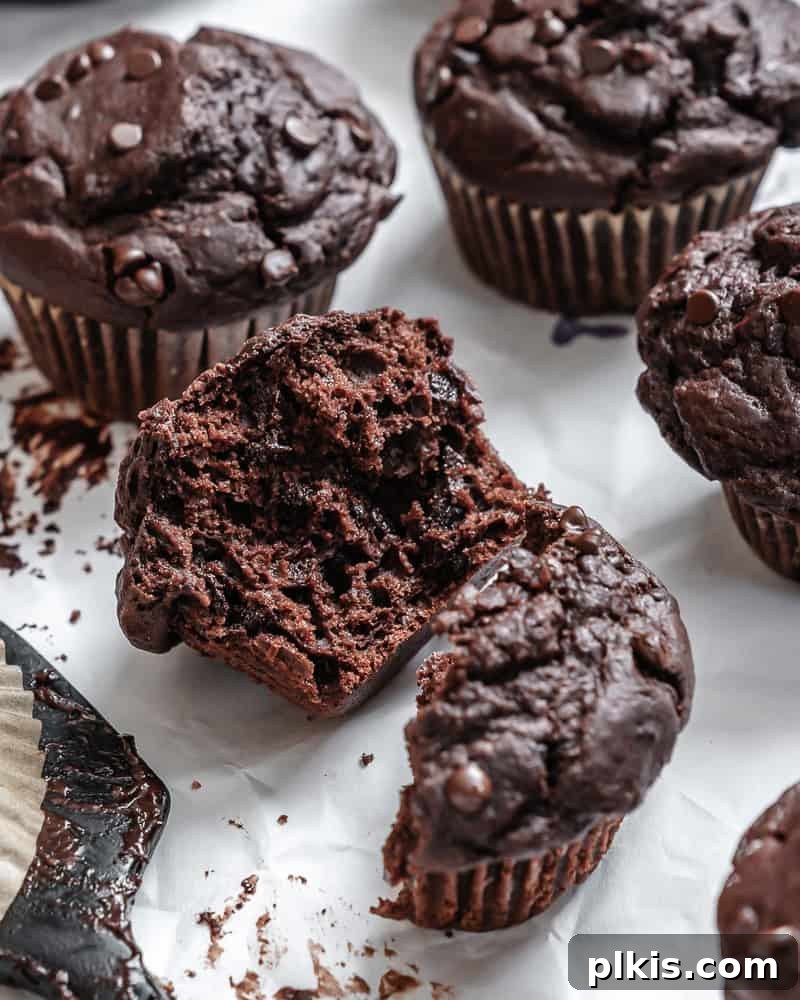 Decadent Double Chocolate Muffins 11 A close-up shot of a vegan chocolate chocolate chip muffin cut in half, revealing its moist interior and melted chocolate chips.