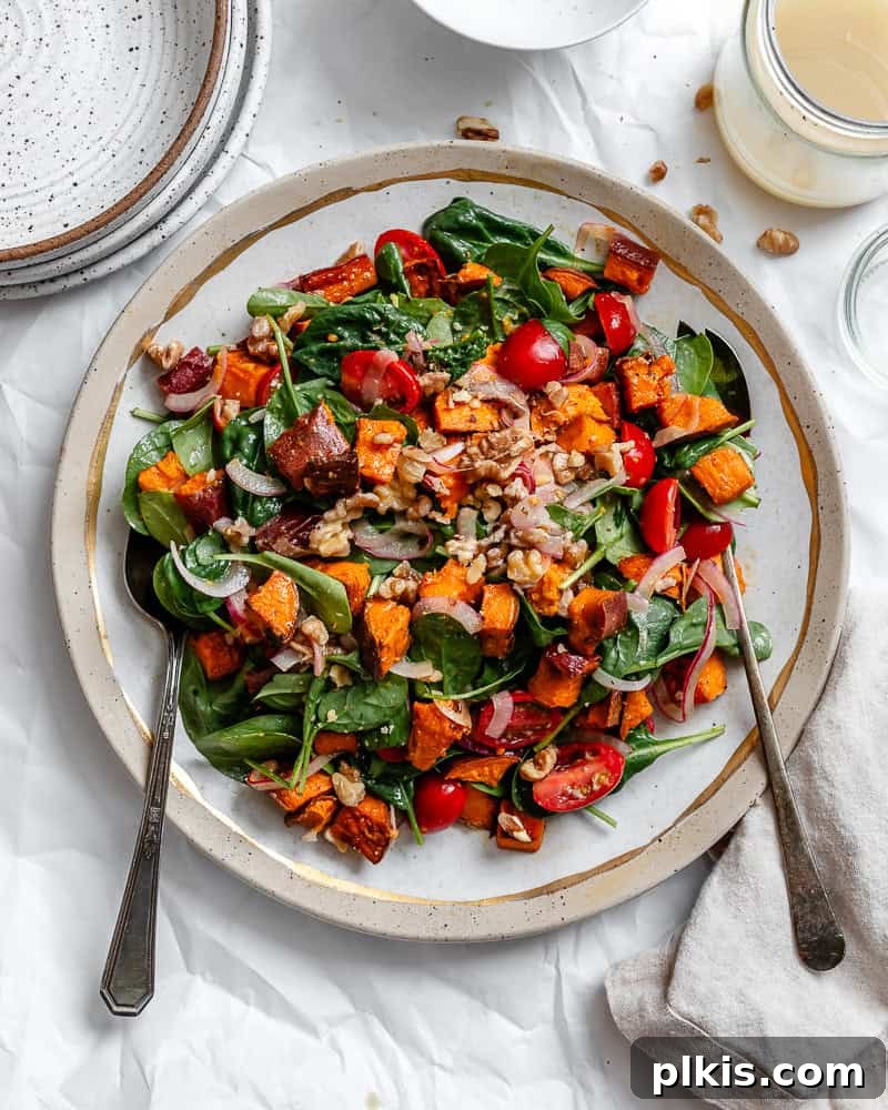Warm Roasted Sweet Potato Salad 2 A vibrant roasted sweet potato salad served on a white plate, garnished with fresh herbs, highlighting perfectly caramelized sweet potato cubes, fresh spinach, and cherry tomatoes.