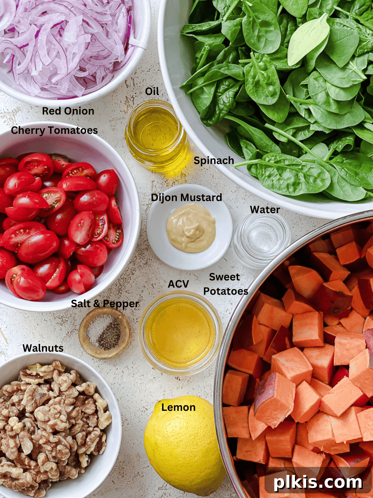 Warm Roasted Sweet Potato Salad 3 An assortment of fresh ingredients laid out, including cubed sweet potatoes, vibrant baby spinach, ripe cherry tomatoes, crunchy walnuts, a lemon, a bottle of olive oil, and apple cider vinegar.