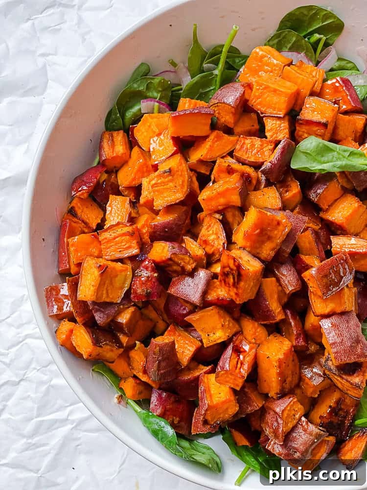 Warm Roasted Sweet Potato Salad 7 Cooked sweet potato cubes being gently added to a bowl with spinach and other salad components.