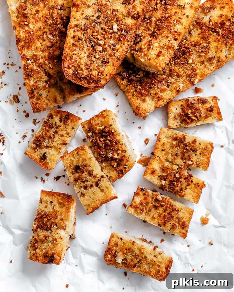 Effortless Plant-Based Garlic Bread 2 Several golden-brown, crispy easy vegan garlic bread slices arranged on a pristine white surface, garnished with fresh parsley.
