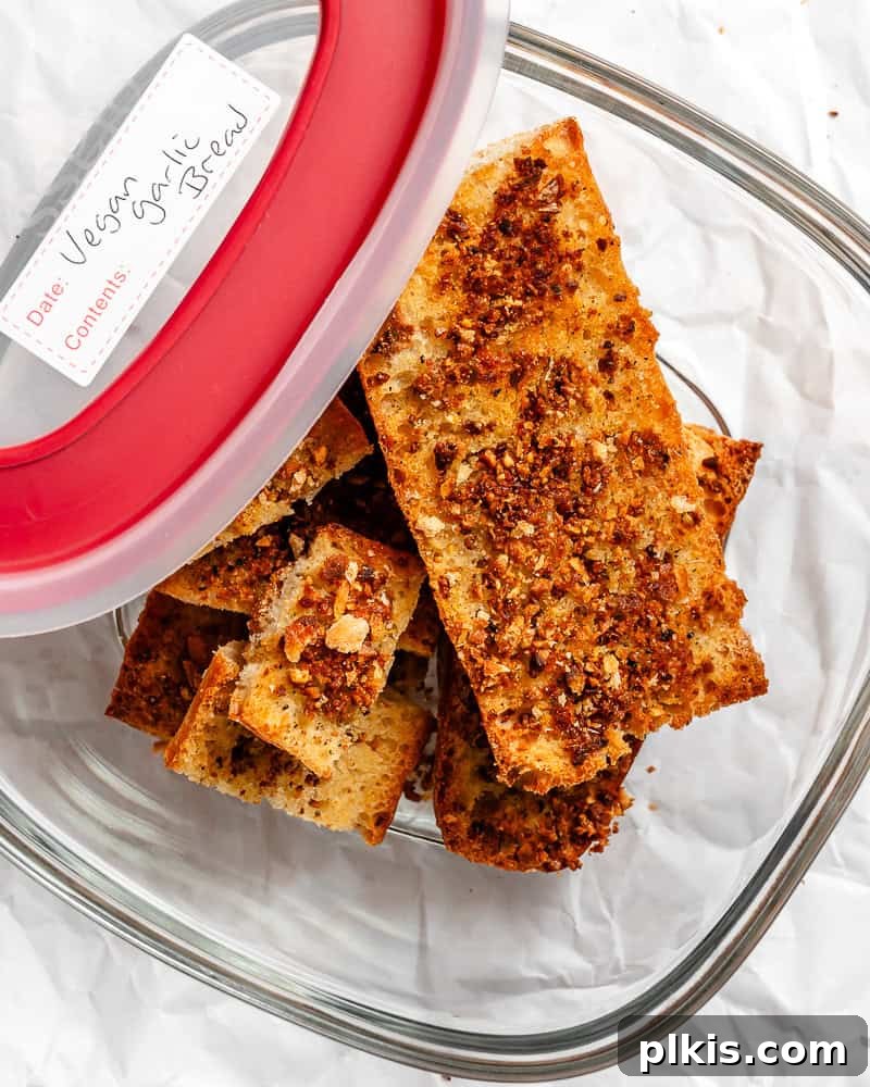 Effortless Plant-Based Garlic Bread 11 Several slices of easy vegan garlic bread neatly stacked inside a clear storage container, ready to be put away.