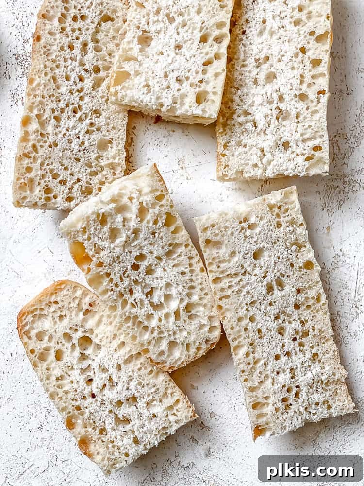 Effortless Plant-Based Garlic Bread 4 Slices of a baguette neatly arranged on a white cutting board, ready for the next step in making vegan garlic bread.