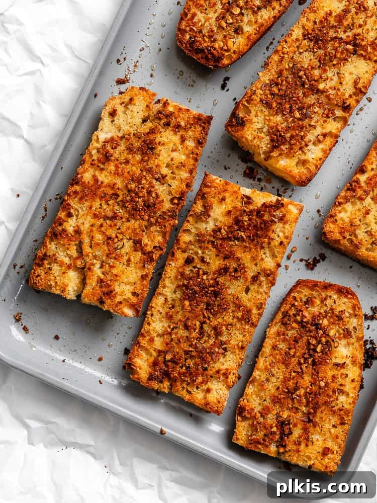 Effortless Plant-Based Garlic Bread 9 Finished easy vegan garlic bread slices, golden and crispy, fresh out of the oven and still on the baking sheet, garnished with fresh herbs.