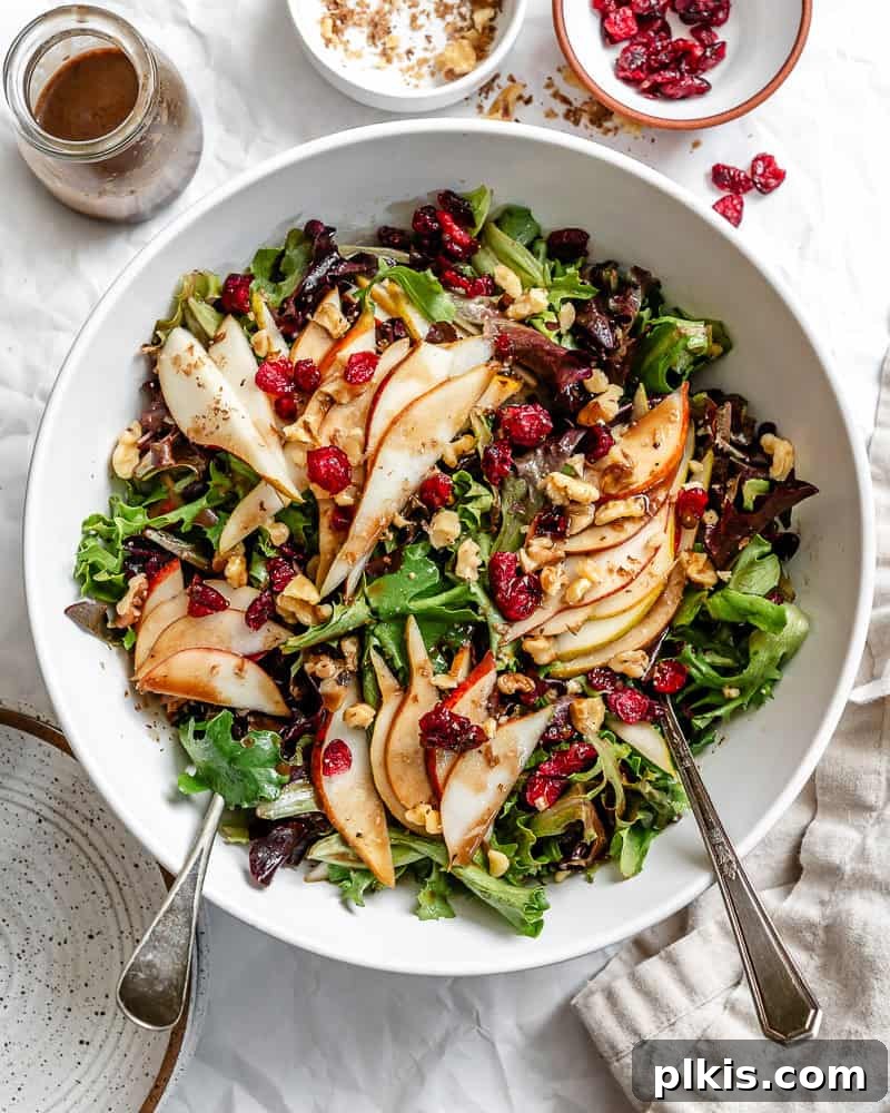 Harvest Pear and Gorgonzola Salad 2 A large bowl filled with a fresh, vibrant pear salad, featuring sliced pears, green leafy vegetables, cranberries, and nuts, all lightly coated in dressing.