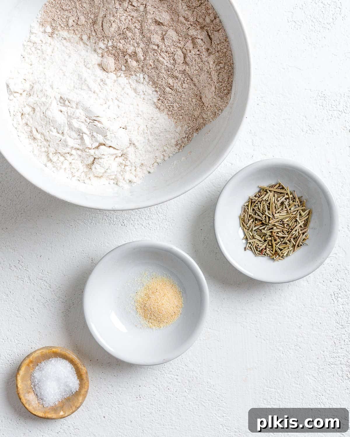 Rustic Rosemary Vegan Crisps 4 Dry ingredients for Rosemary Vegan Crackers measured out in small white bowls on a white surface.