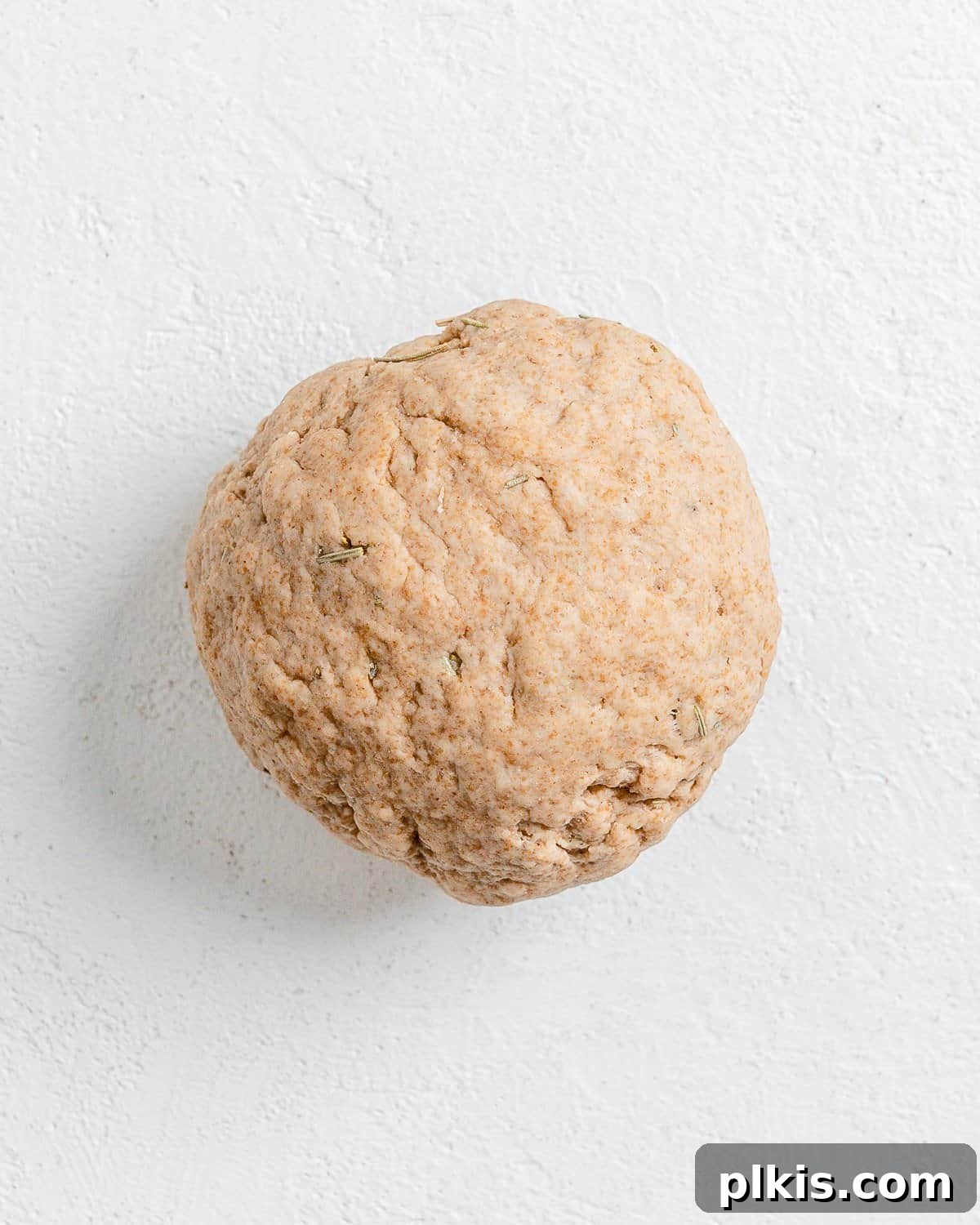 Rustic Rosemary Vegan Crisps 7 The process of forming the cracker dough into a ball on a white surface.