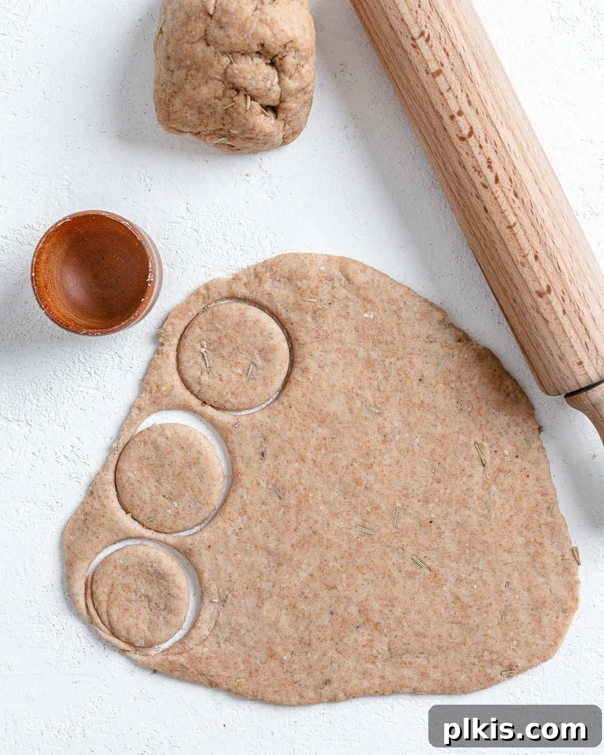 Rustic Rosemary Vegan Crisps 8 Process of using a circular cookie cutter to cut dough shapes on a white surface.