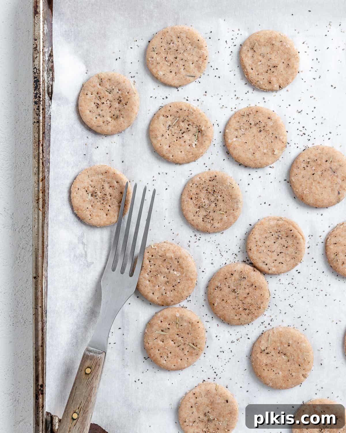 Rustic Rosemary Vegan Crisps 9 Process of placing cut cracker dough onto a white baking sheet, prepared for baking.