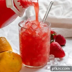 A glass of vibrant Fresh Strawberry Lemonade, garnished with a sliced strawberry and lemon wedge, ready to be served.