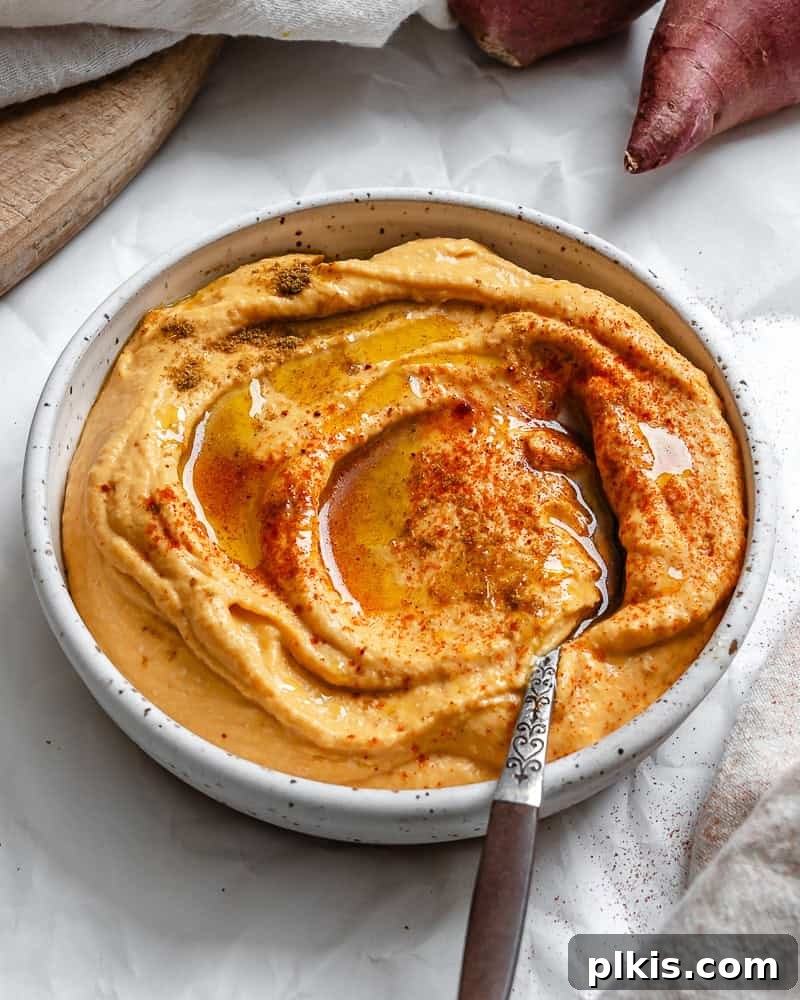 Golden Sweet Potato Hummus 2 A bowl of vibrant orange sweet potato hummus garnished with fresh herbs and a drizzle of olive oil, ready for serving.