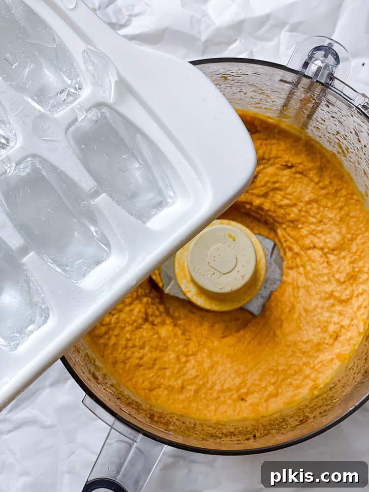 Golden Sweet Potato Hummus 8 Ice cubes being added to the partially blended sweet potato hummus in a food processor.