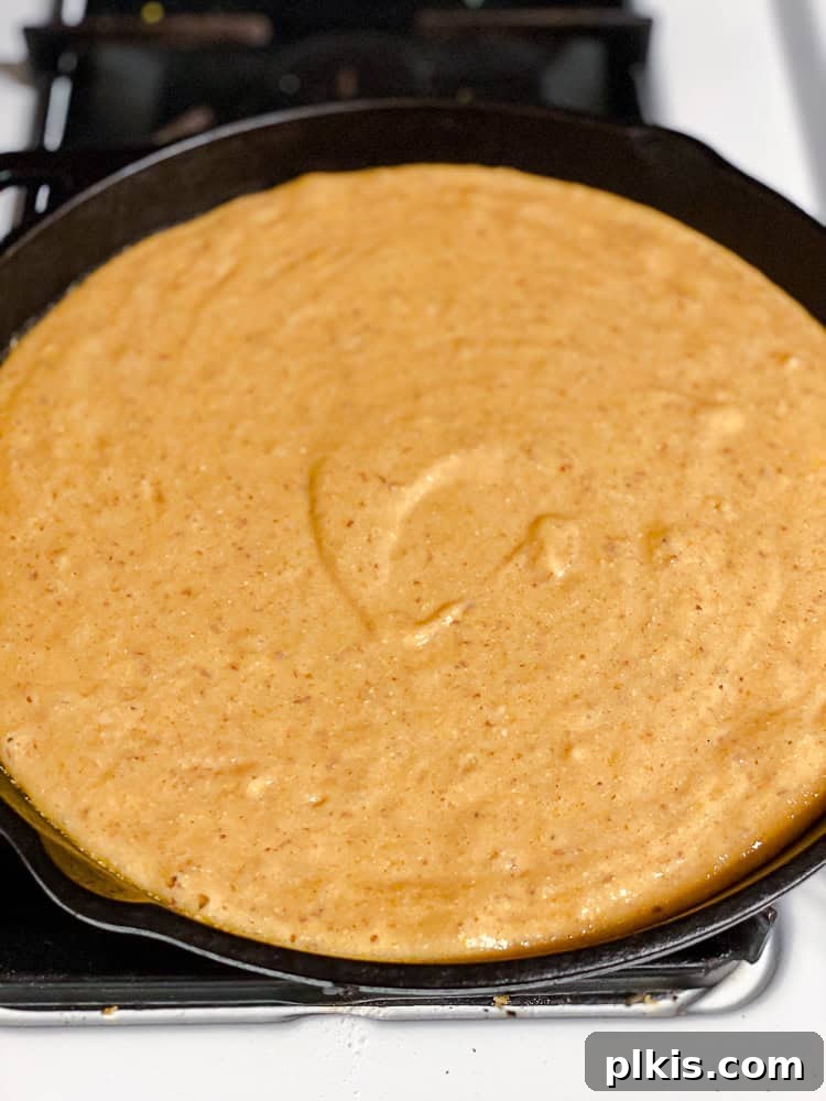 Spiced Sweet Potato Cornbread 9 Raw sweet potato cornbread batter spread evenly in a hot cast-iron skillet, ready for baking.
