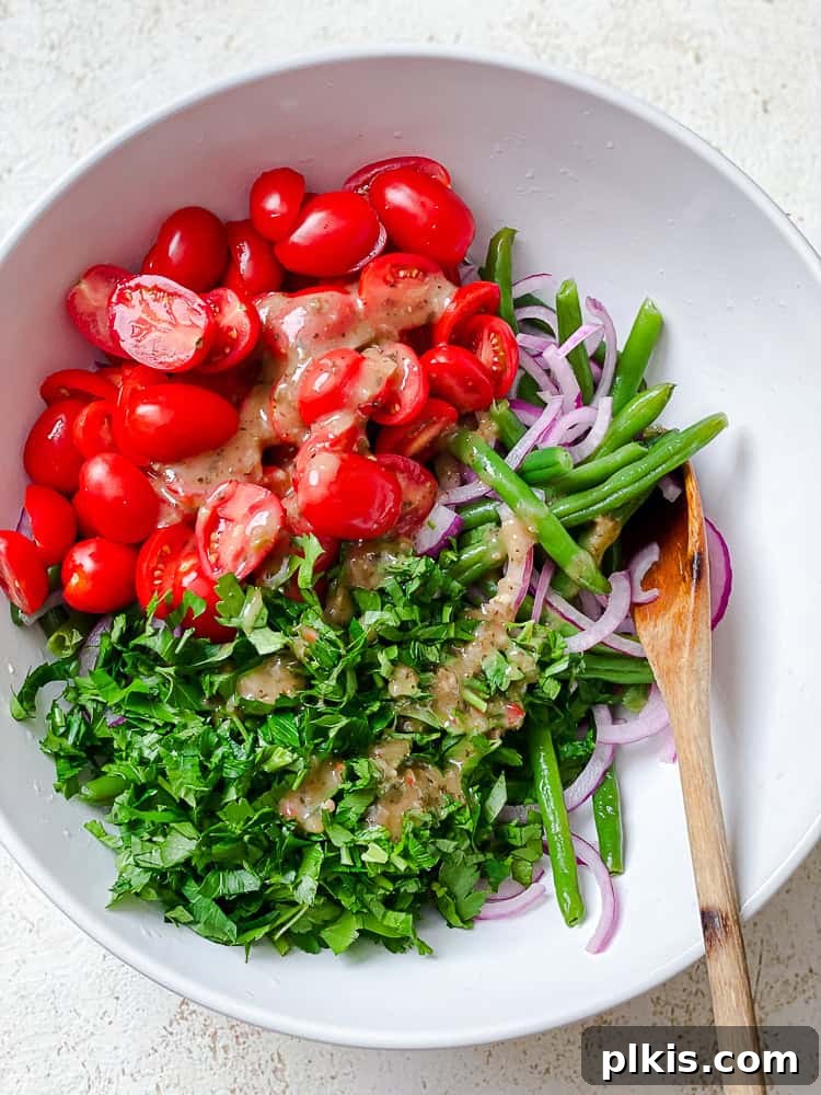 Zesty Green Bean Salad 6 process shot showing green beans, tomatoes, parsley, and onion in a bowl