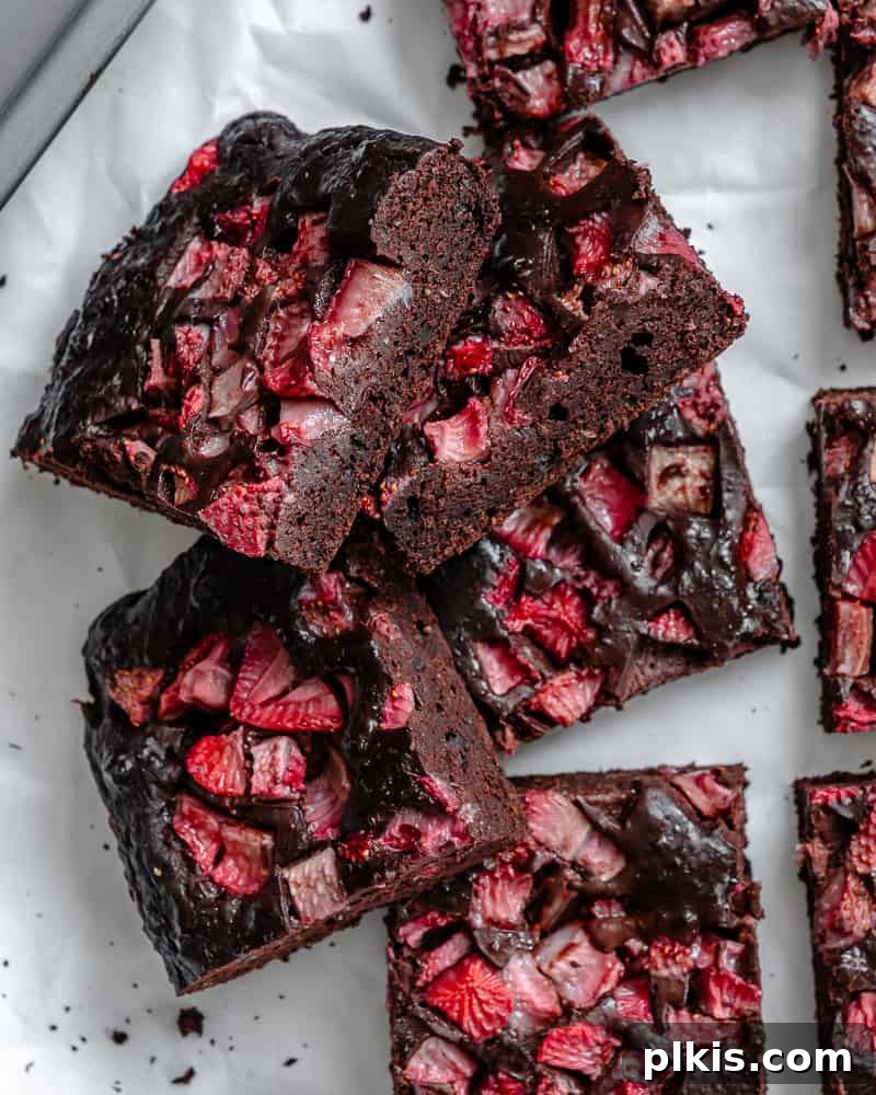 Strawberry Kissed Brownies 2 Fudgy Strawberry Brownies with fresh strawberries on top, resting on a white surface, ready to be served.