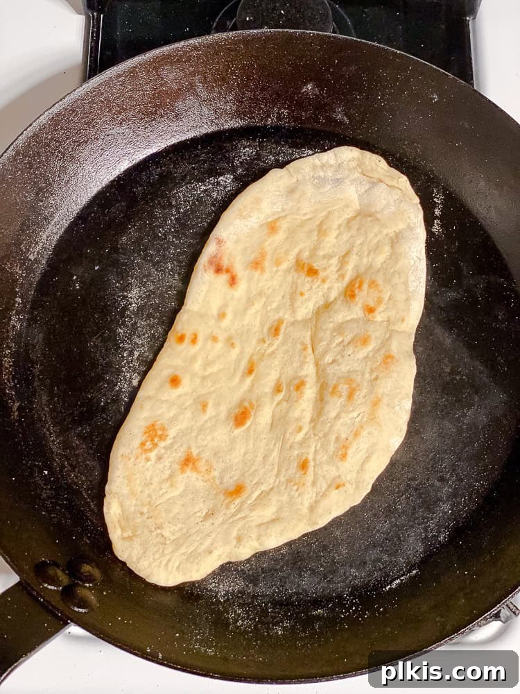 Fluffy Vegan Naan 14 A piece of vegan naan dough cooking in a hot black cast iron skillet, bubbling and charring.