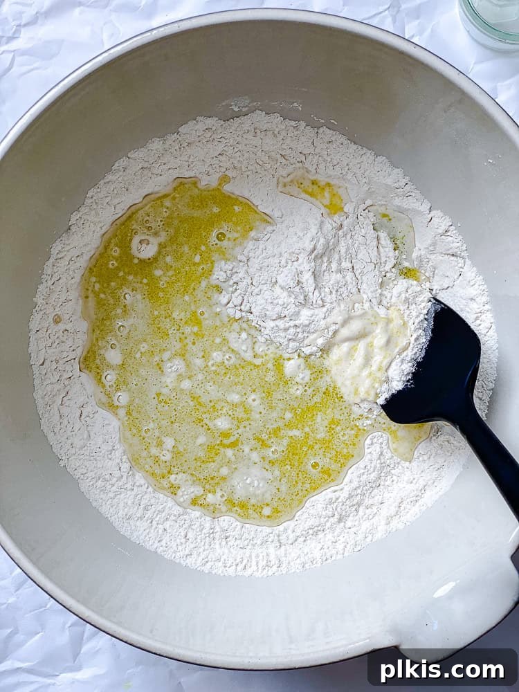 Fluffy Vegan Naan 8 A black spatula stirring together wet and dry ingredients in a white bowl, forming a sticky dough.