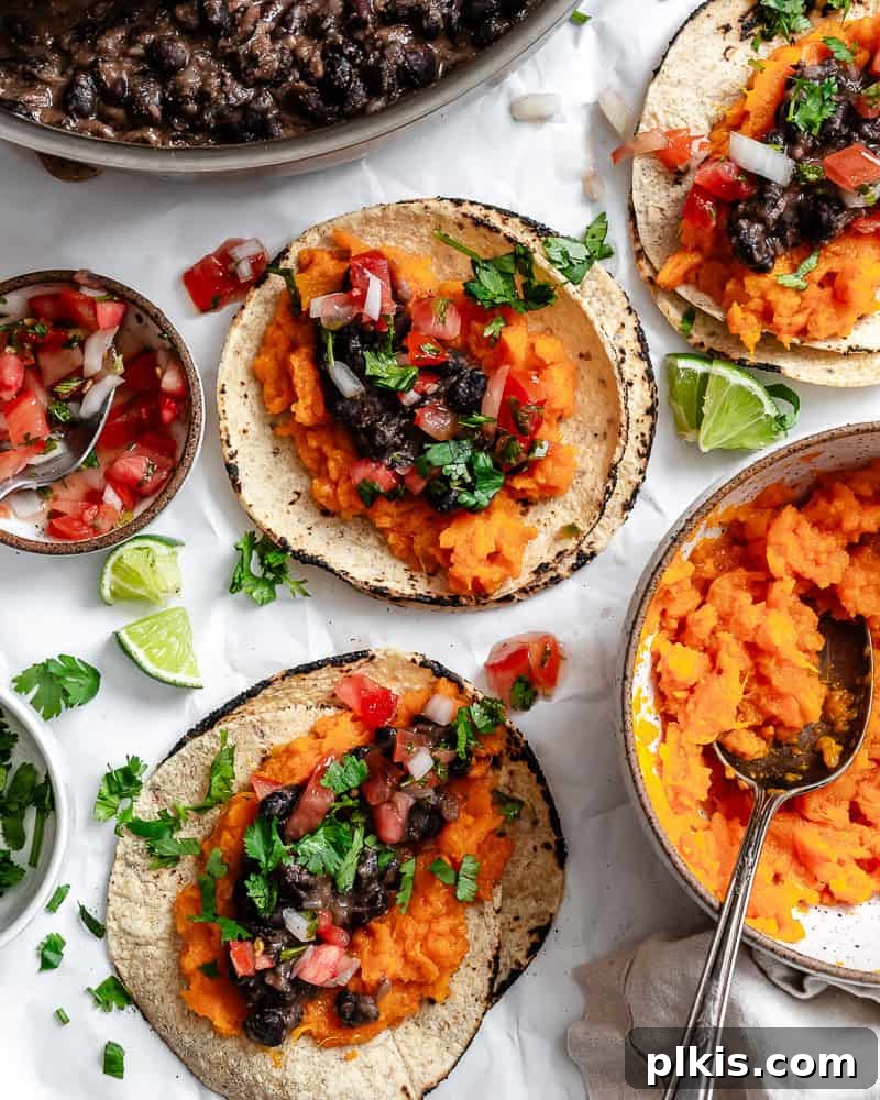 Hearty Sweet Potato Black Bean Tacos 2 Several vibrant Sweet Potato and Black Bean Tacos arranged beautifully on a white surface, garnished with fresh cilantro and lime wedges.