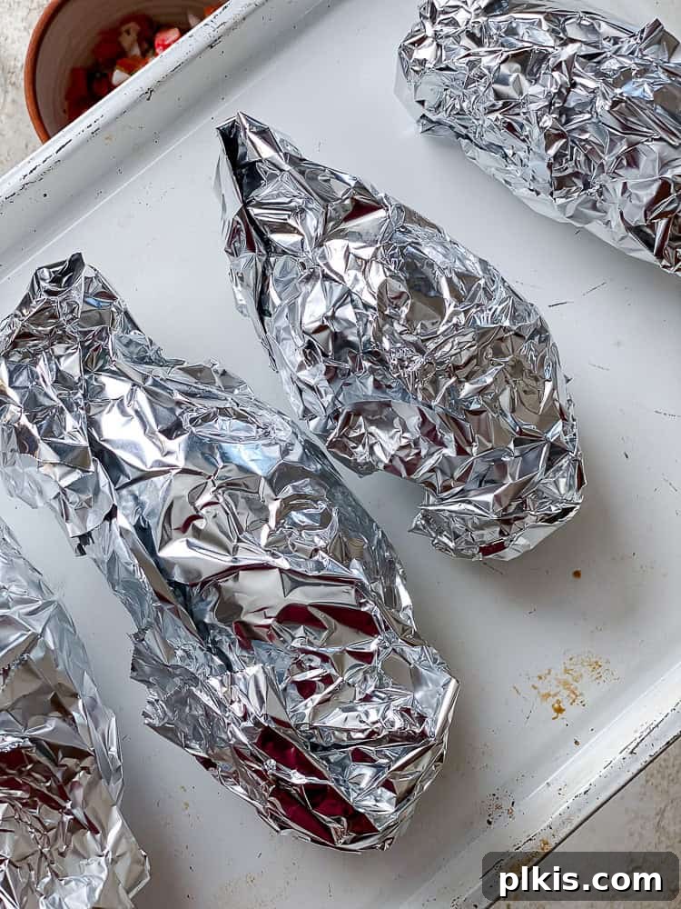 Hearty Sweet Potato Black Bean Tacos 4 Two sweet potatoes wrapped in aluminum foil, ready for baking on a baking sheet.