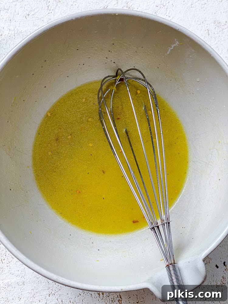 Zesty Zucchini Salad 4 A hand whisking the homemade dressing ingredients in a large white bowl.