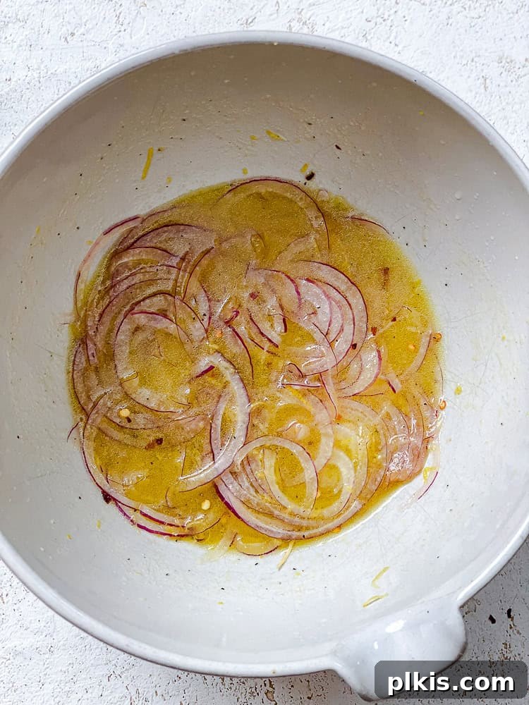 Zesty Zucchini Salad 5 Thinly sliced red onions are tossed in the homemade dressing within a large white bowl.