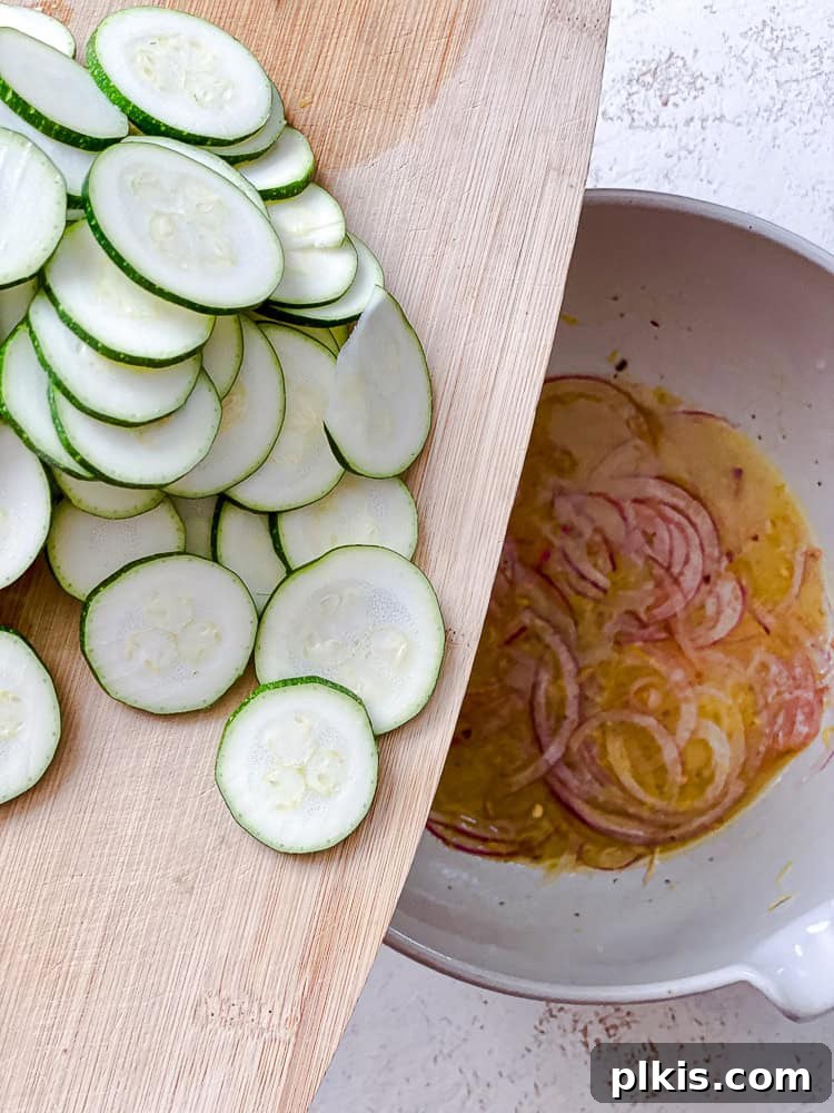 Zesty Zucchini Salad 6 A hand holds thinly sliced zucchini above a bowl containing the dressing and red onions, ready to be added.