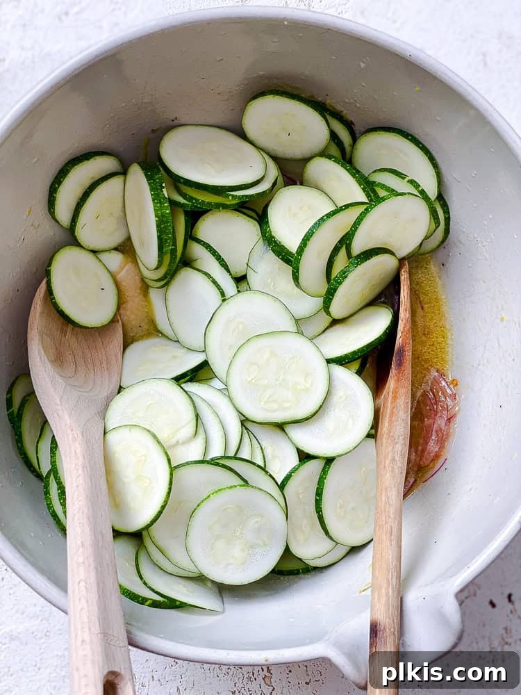 Zesty Zucchini Salad 7 Two wooden spoons gently toss zucchini slices in a large white bowl with the dressing and onions.