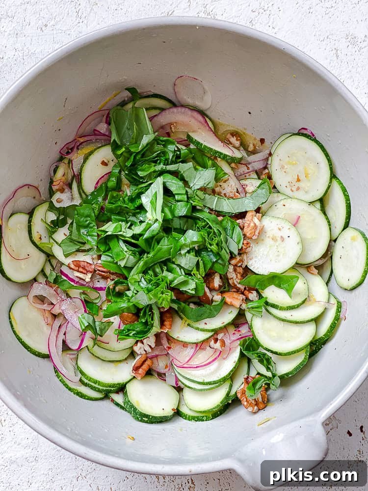 Zesty Zucchini Salad 8 All the zucchini salad ingredients, including nuts and basil, are gathered in a large white bowl, ready for a final toss.
