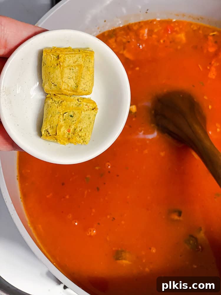 Tuscan Vegan Lasagna Soup 8 Two vegetable bouillon cubes being added to a pot of simmering vegan lasagna soup ingredients.