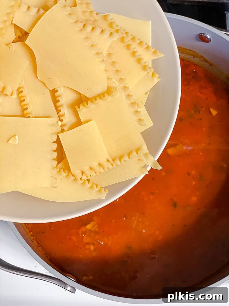 Tuscan Vegan Lasagna Soup 10 A bowl of broken lasagna noodles being poured into a pot of vegan lasagna soup.