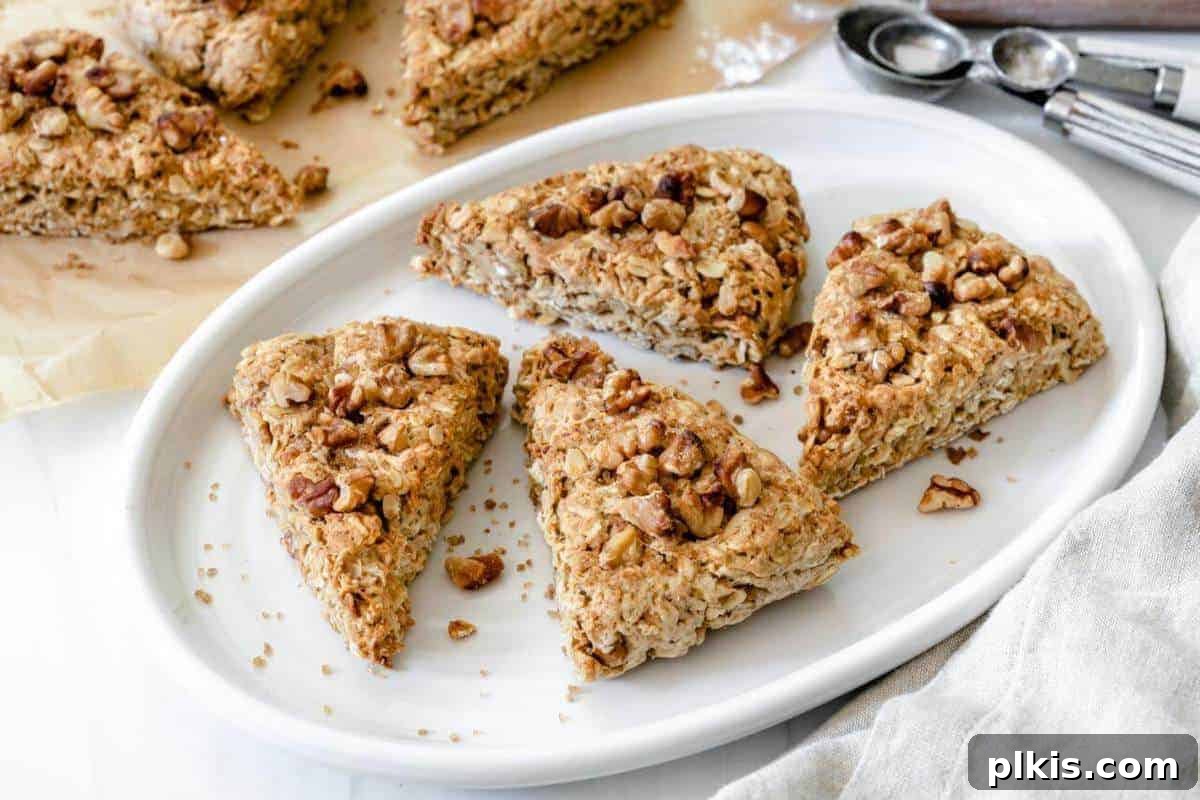 4 vegan walnut oat scones arranged on a pristine white platter, with more scones softly blurred in the background, inviting a closer look at their golden-brown perfection.