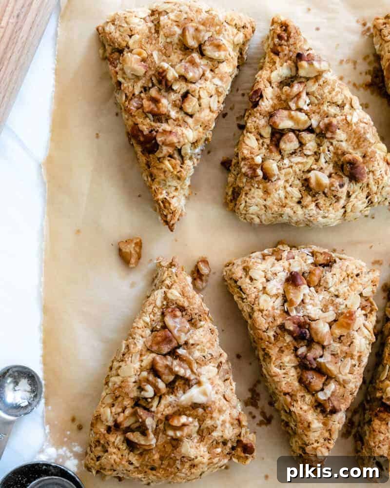 Five perfectly baked walnut oat scones stacked on a white tray, with a rustic, warm backdrop suggesting a cozy kitchen setting.