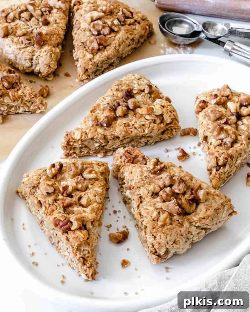 A close-up shot of five warm, freshly baked walnut oat scones sitting on a clean white tray, with a softly blurred background hinting at more culinary delights.
