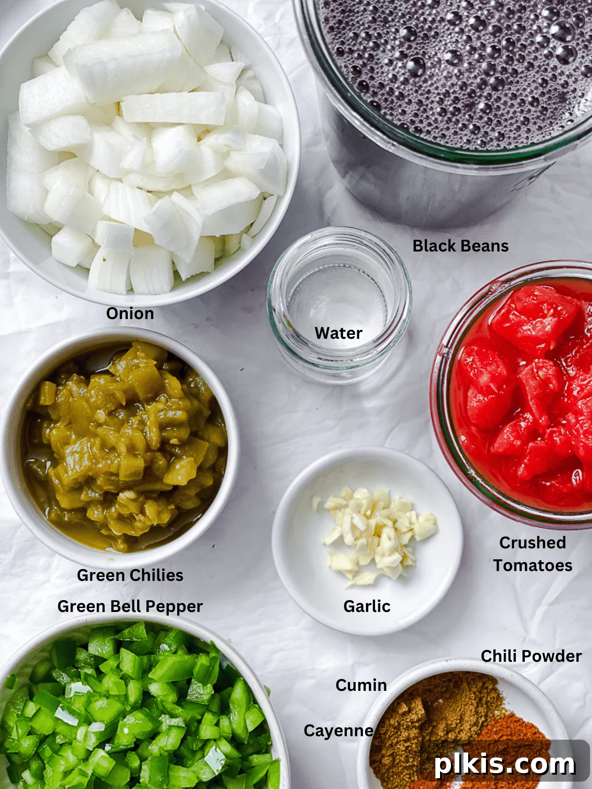 A colorful array of fresh and canned ingredients for black bean chili, including black beans, crushed tomatoes, bell peppers, onions, garlic, and various spices.