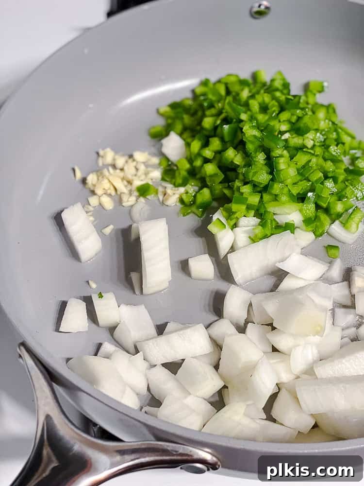 process shot showing diced onions, garlic, and bell pepper cooking in a pan with water.