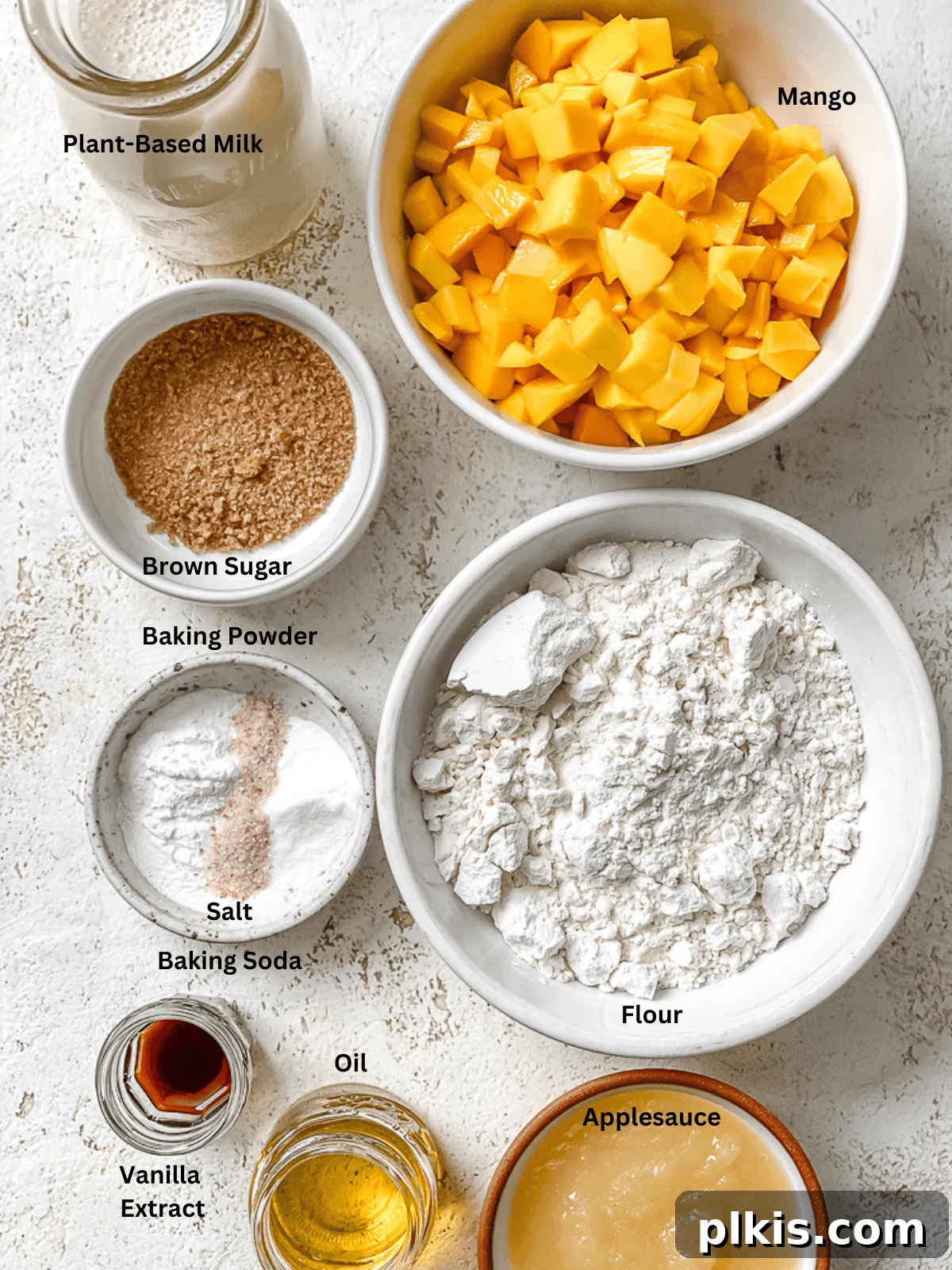 Golden Mango Cloud Cakes 3 Separated ingredients for fluffy mango pancakes laid out on a white surface, showcasing fresh mango, flour, milk, and other components.