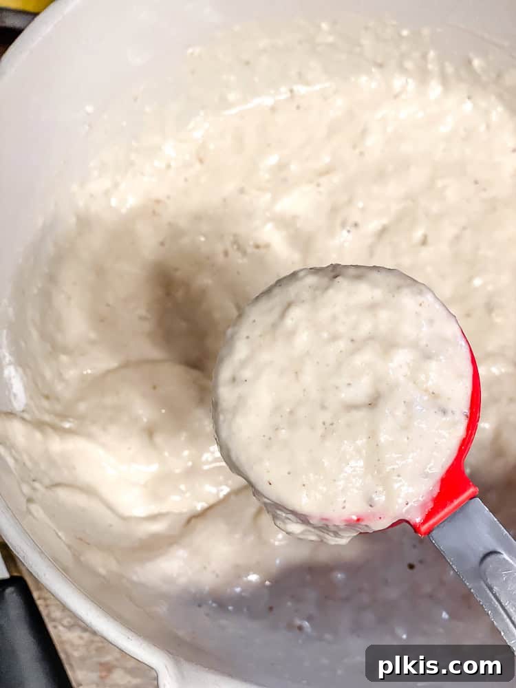 Golden Mango Cloud Cakes 6 Process shot of pancake batter being scooped into a measuring cup for precise portioning.