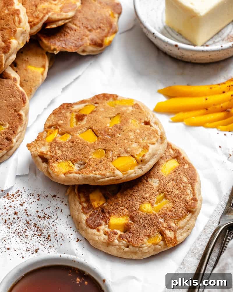 Golden Mango Cloud Cakes 8 A stack of perfectly cooked fluffy mango pancakes on a white plate, ready to be served.
