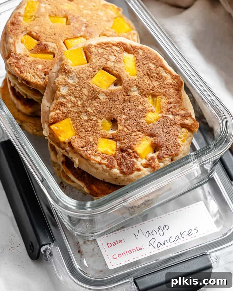 Golden Mango Cloud Cakes 9 Fluffy mango pancakes neatly stacked in an airtight storage container, separated by parchment paper.