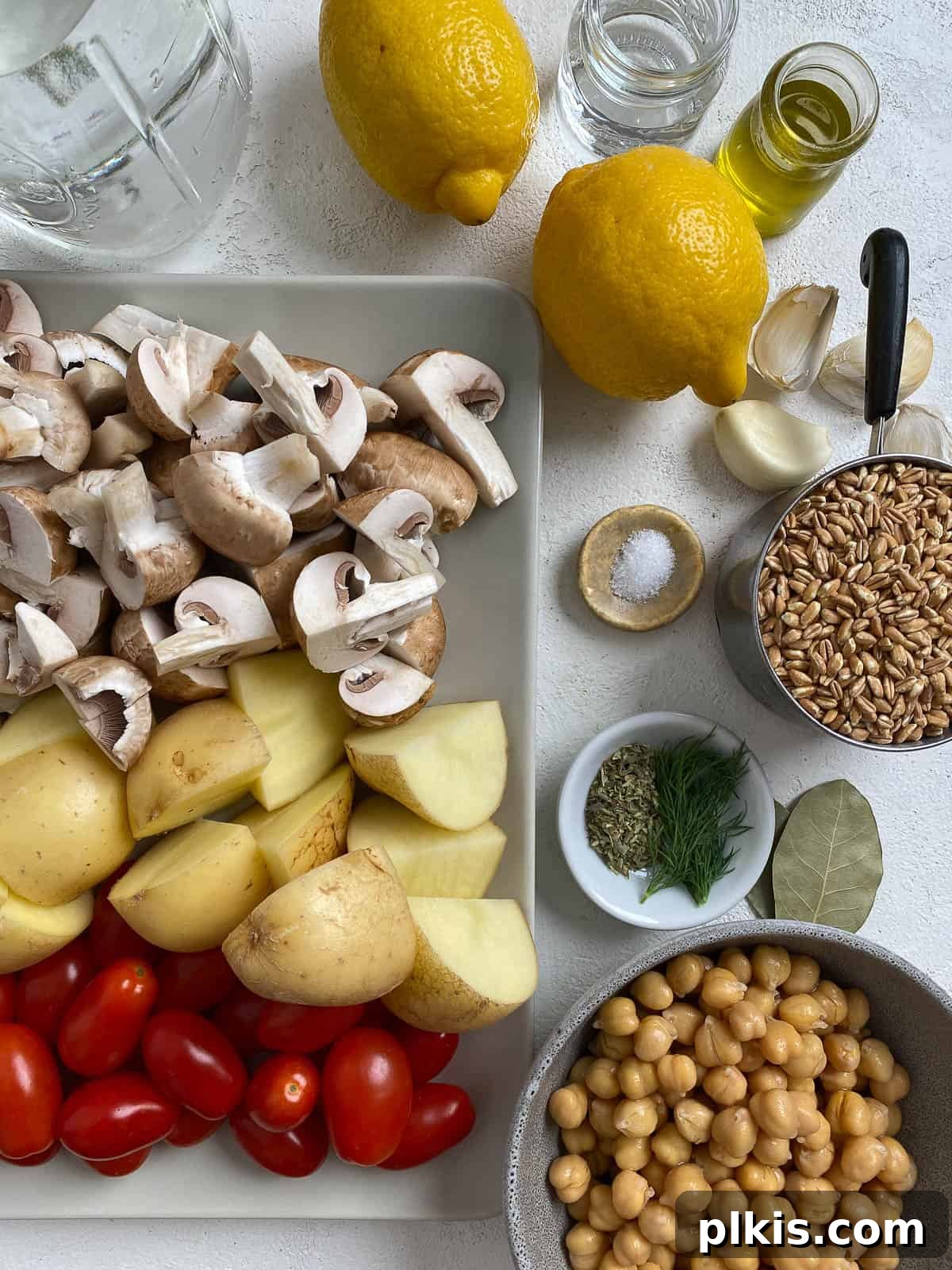 Ingredients for Easy Farro Recipe with Roasted Vegetables measured out against a white surface, including potatoes, tomatoes, mushrooms, and herbs