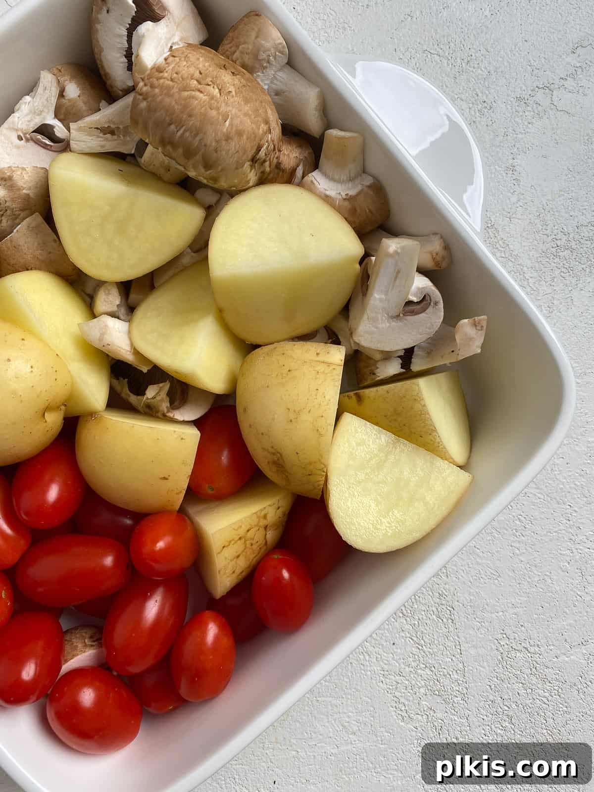 Ingredients for Easy Farro Recipe with Roasted Vegetables added to a dish, showing potatoes, tomatoes, and mushrooms