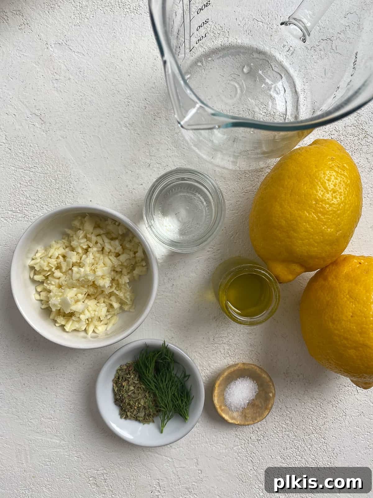 Ingredients for Easy Farro Recipe with Roasted Vegetables measured out against a white surface, specifically showcasing liquids and herbs