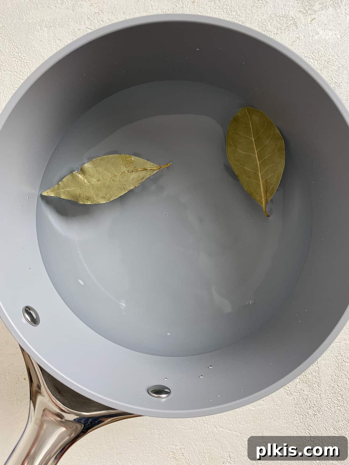 Two bay leaves added to a pan of water, preparing to cook farro