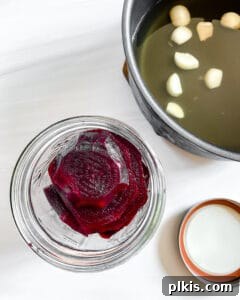 Jar of Small Batch Pickled Beets with a pot of brine ingredients in the background, showing the process of combining.