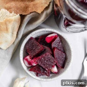Completed Small Batch Pickled Beets in a small bowl and mason jar against a white background with several ingredients in the background