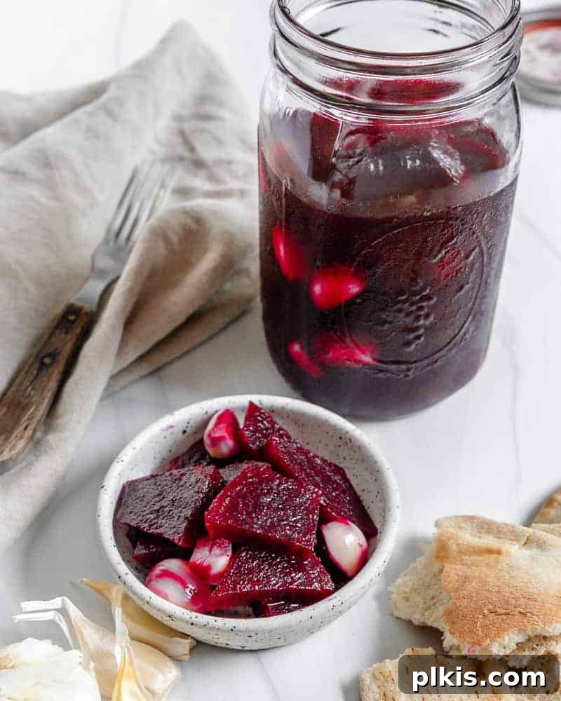 Completed Small Batch Pickled Beets in a small bowl and mason jar against a white background with several ingredients in the background, showing their readiness to be served.