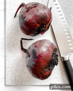 Two whole beets with a knife against a white background, demonstrating the peeling stage.